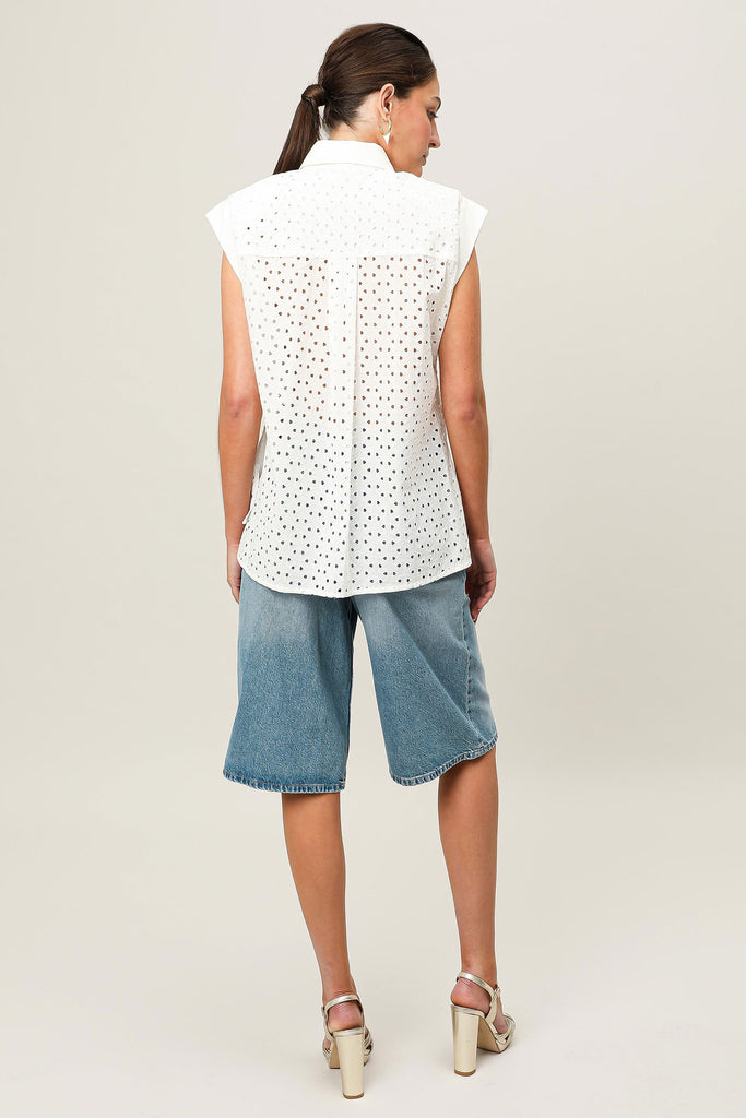 Model wearing the Aura State embroidered anglaise shirt with cotton stretch sateen panelling detailing by Realm Origin, shown from the back to highlight the shoulder pads and contrast cotton fabrication, styled with denim shorts and heels against a neutral background.