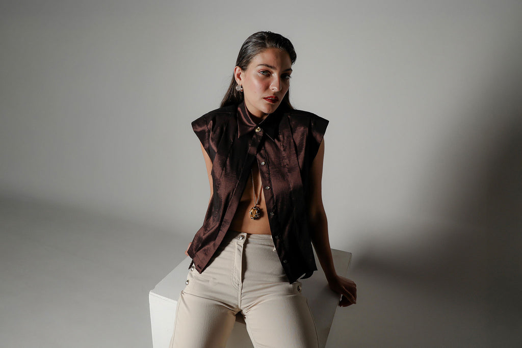 Campaign editorial shot of the Realm Origin Sol Verite Shirt in mocha brown, styled on a model in a seated pose to highlight the structured shoulders, flange pleats and modern tailored silhouette.